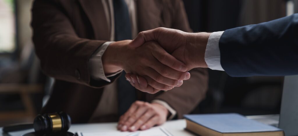 Two formally dressed people shake hands above desktop
