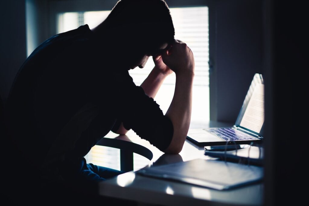 A stressed person resting head on hands while sitting at a desk