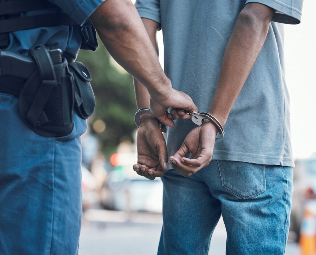 Police man holding hands of someone in handcuffs behind back