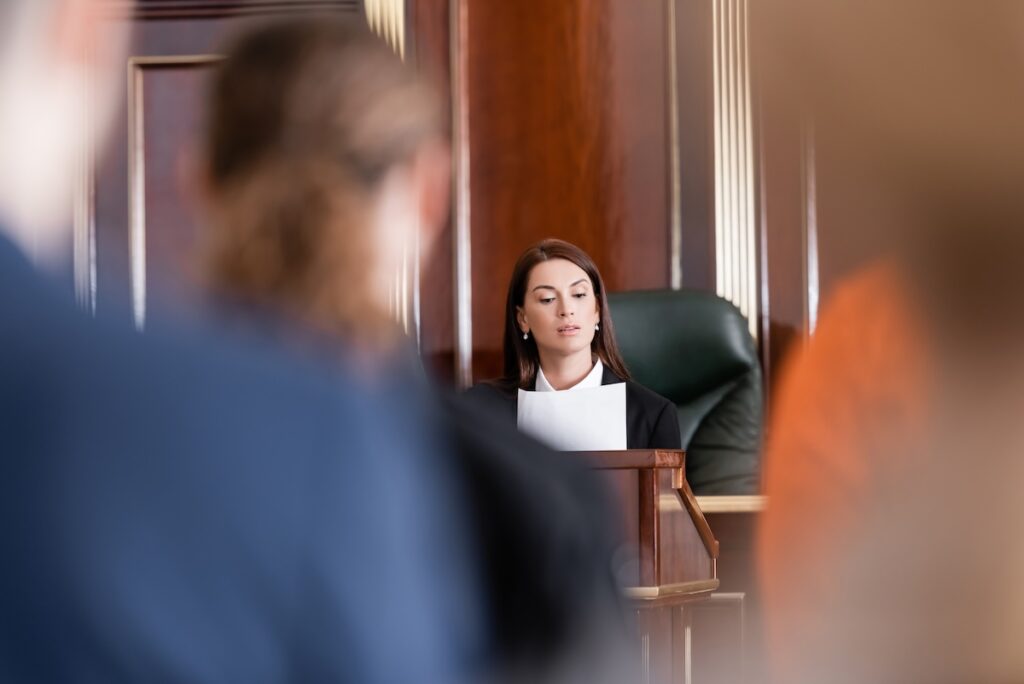 prosecutor reading lawsuit in court near people on blurred foreground